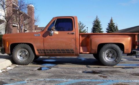 1979 Chevrolet C/K Pickup - This orange pickup truck is parked in a lot with some puddles on the ground.