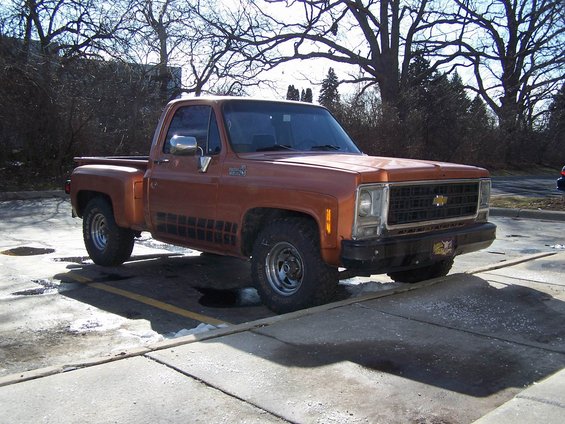 Orange pickup truck parked in a lot. It has a black grille and black trim on the side