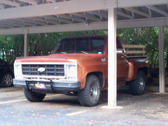 Orange pickup truck parked under a carport, showing front grille, bumper, and side profile