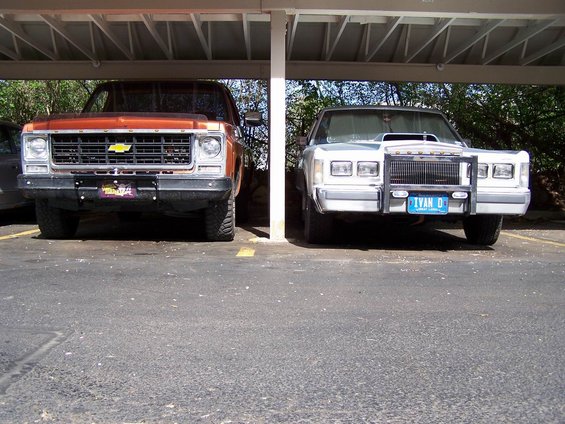Orange truck with a yellow Chevy bowtie grille and a white truck with a blue license plate that says 'IVAN D'