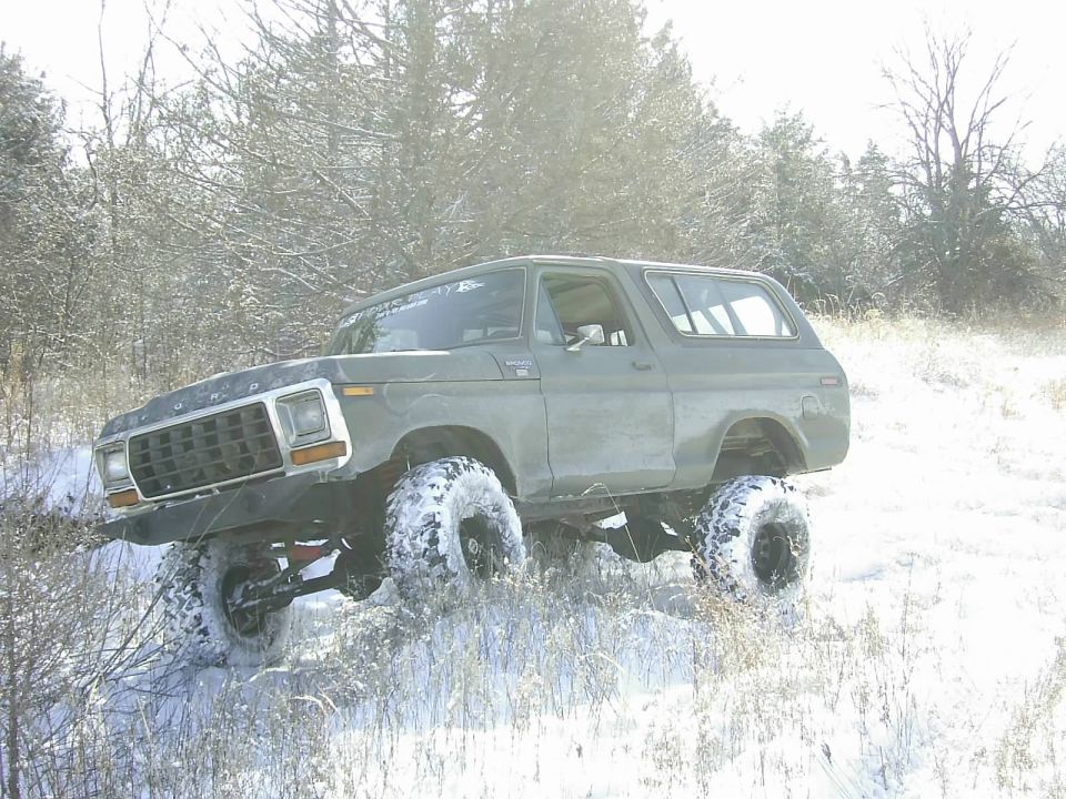 Olive green 1978 Ford Bronco with large tires driving in snow