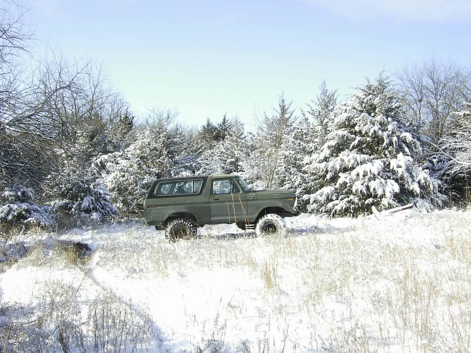 Green 1978 Ford Bronco parked in a snowy field with snow-covered trees