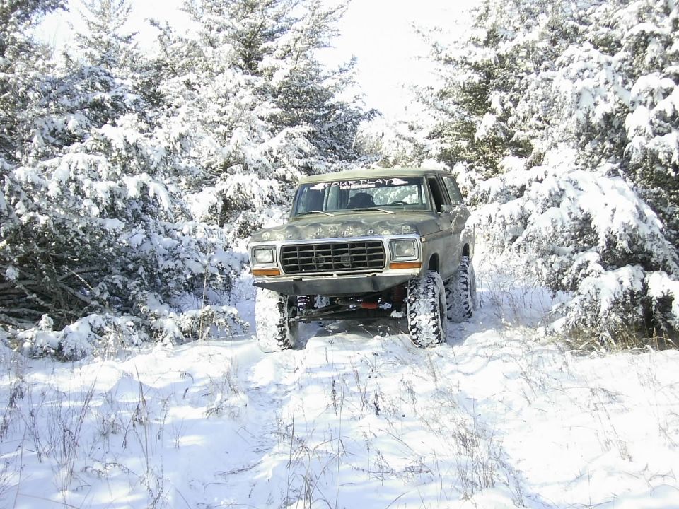 1978 Ford Bronco driving on a snowy trail with trees covered in snow