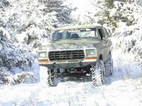 1978 Ford Bronco - A lifted 1978 Ford Bronco navigates a snow-covered trail surrounded by snow-laden trees.