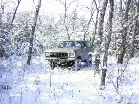 1978 Ford Bronco - A lifted 1978 Ford Bronco navigates a snow-covered forest with large, aggressive tires.