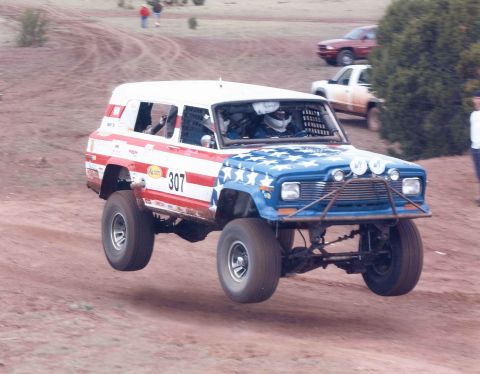 1990 Ford Bronco - An off-road vehicle with a patriotic paint scheme jumps over a dirt track during a race.