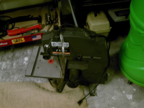 1986 Ford Bronco - A black table saw sits on a concrete floor next to a green object and some tools.