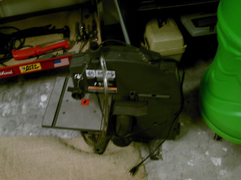 Benchtop band saw on a garage floor with coiled spare blades and tools around it