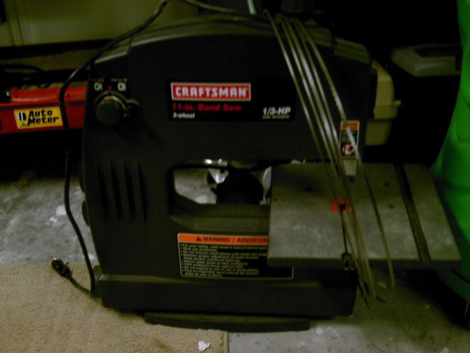 Craftsman 11-inch 1/3-HP band saw on a floor with spare blades coiled over it