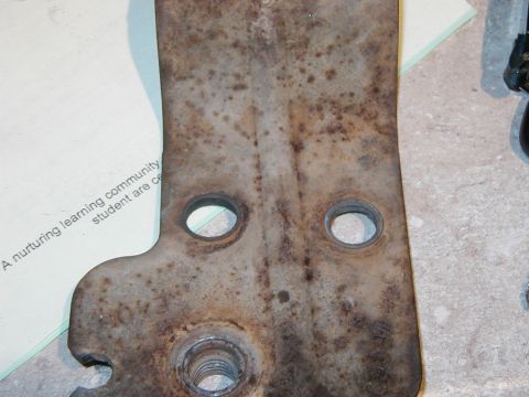 1993 Ford Bronco - A heavily rusted metal component with visible holes and threaded sections, partially covered by a document.