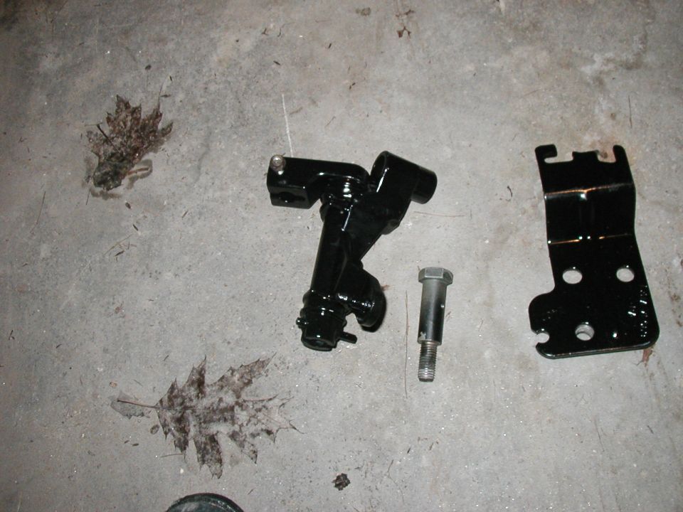 Black metal shifter linkage components and a bolt on a concrete floor with fallen leaves