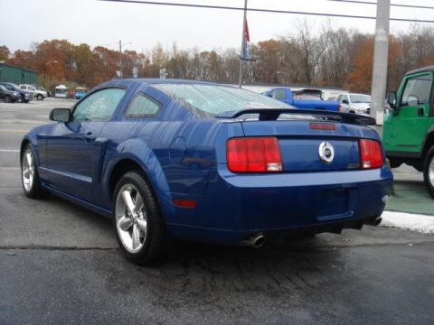 2007 Ford Mustang - A blue Ford Mustang coupe is parked on wet pavement, with other vehicles visible in the background.