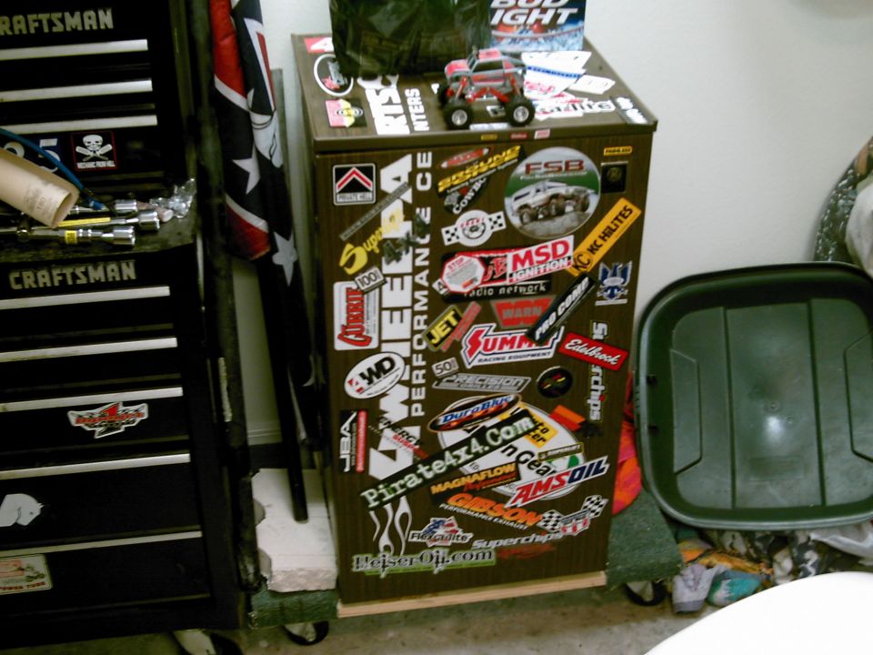 Sticker-covered rolling garage cabinet with RC crawler on top beside Craftsman tool chest