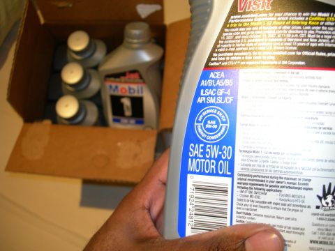 1992 Ford Taurus - A hand holds a bottle of Mobil 1 5W-30 motor oil, with several other bottles visible inside a cardboard box.