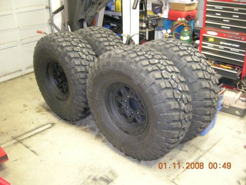 1996 Ford Bronco - Four off-road tires and wheels are stored in a garage setting.