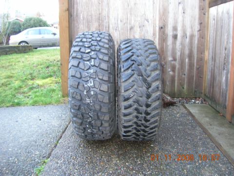 1996 Ford Bronco - Two off-road tires are displayed side-by-side on a paved surface with a wooden fence in the background.