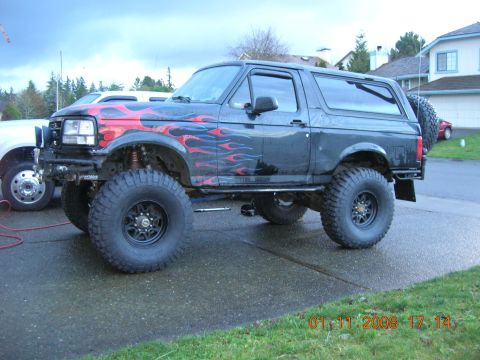 1996 Ford Bronco - This modified SUV features custom flame graphics and oversized tires, parked on a wet driveway.