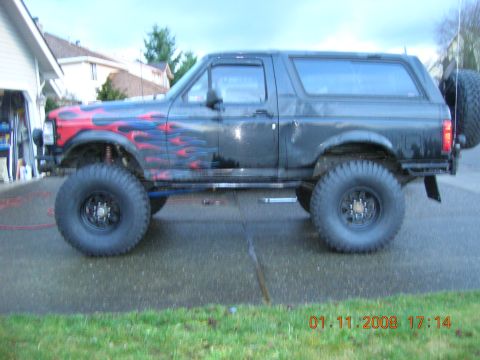 1996 Ford Bronco - Modified black Ford Bronco with flame decals sits on a wet driveway.