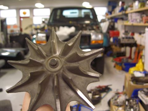 1996 Ford Bronco - A metal impeller part is held in the foreground, with a vehicle in a workshop in the background.