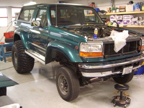 1996 Ford Bronco - A green 1996 Ford Bronco is shown in a garage with its hood open, revealing the engine compartment.