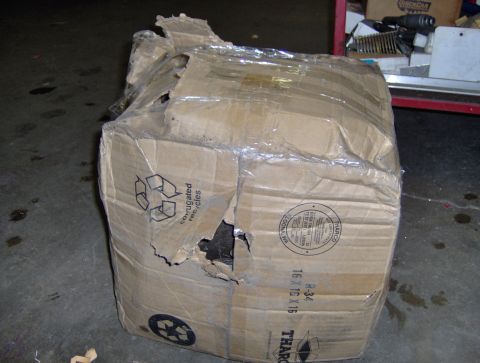 1978 Ford Bronco - A damaged cardboard box sits on a concrete floor, partially wrapped in plastic and showing signs of wear and tear.