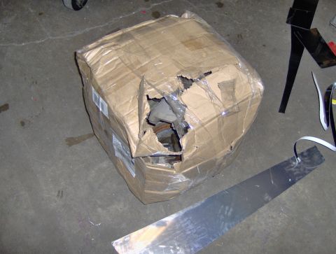 1978 Ford Bronco - A damaged cardboard box, likely containing vehicle parts, sits on a concrete floor with debris scattered around.