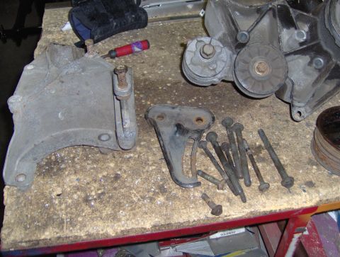 1978 Ford Bronco - Various engine components and fasteners are arranged on a cluttered surface, possibly for repair or replacement.