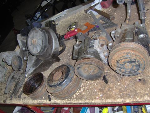 1978 Ford Bronco - Various automotive parts, including pulleys and compressors, are laid out on a workbench alongside tools.