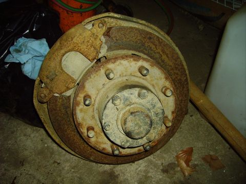 1991 Ford Bronco - This heavily rusted brake drum and caliper assembly is a close-up view of a vehicle part.