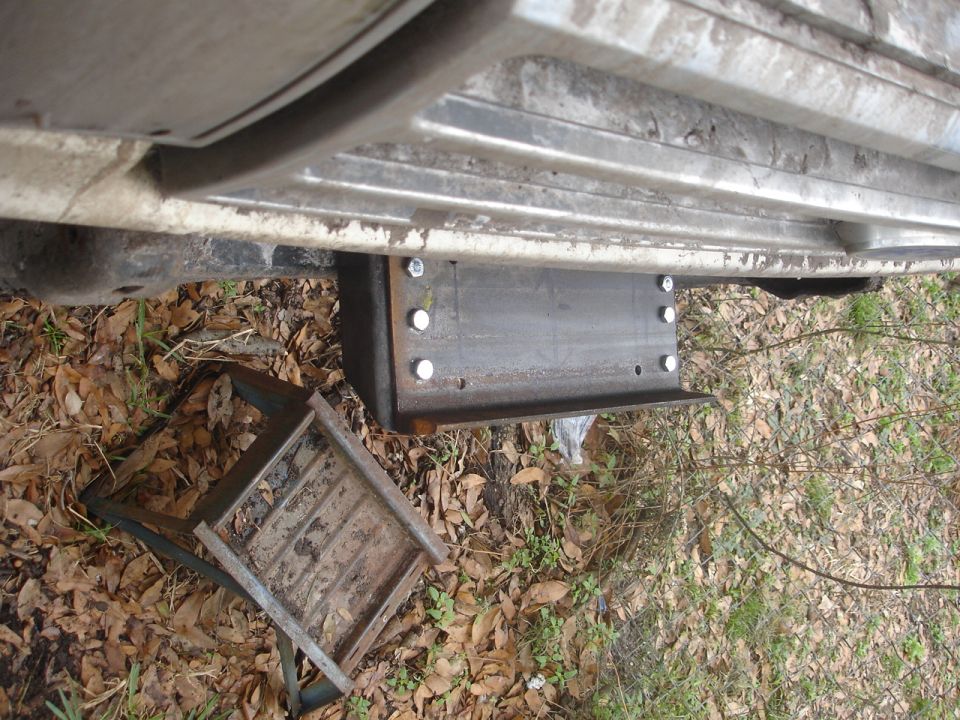 custom steel bracket bolted to vehicle frame, with a metal step or skid plate nearby on the ground
