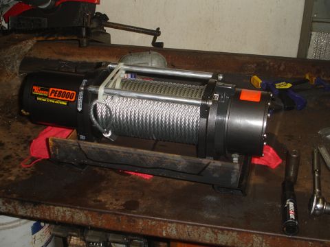 1989 Ford Bronco - A winch with a steel cable is mounted on a workbench, ready for installation.