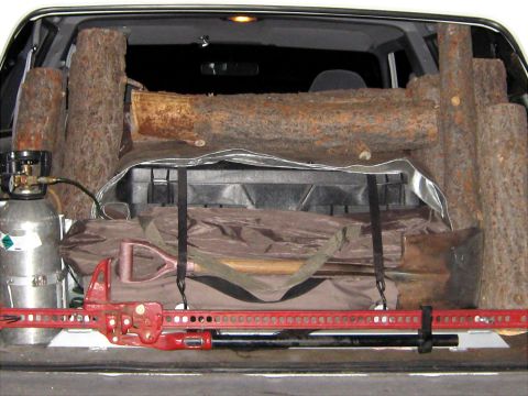 1996 Ford Bronco - Vehicle's cargo area is filled with logs, a shovel, and a hi-lift jack, suggesting preparation for an outdoor activity.