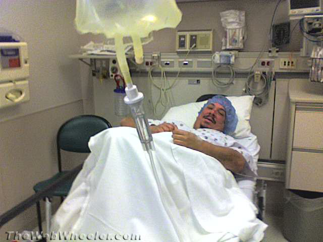 Man in hospital bed with IV drip, wearing a surgical cap