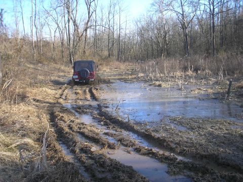 2002 Ford Sport Trac - Jeep Wrangler off-roading through a muddy, wooded area.