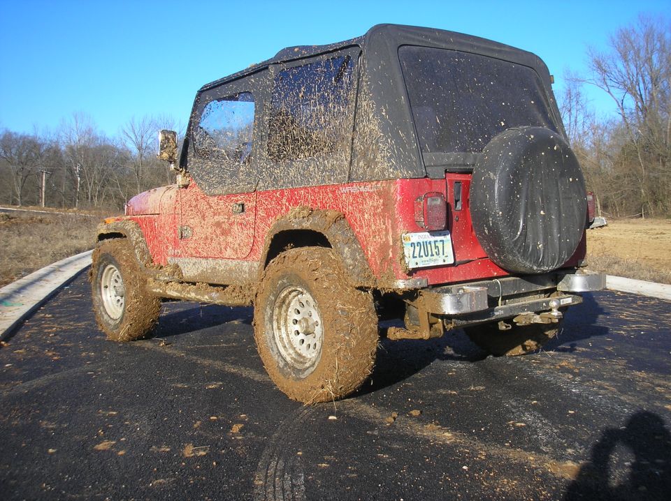 Muddy red Jeep Wrangler parked on asphalt, spare tire on back