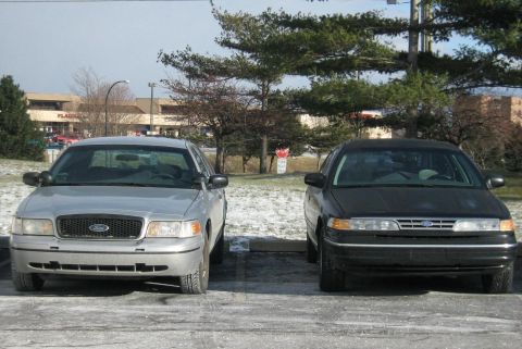 1988 Mercury Grand Marquis - Two sedans, one silver and one black, are parked in a lot with snow on the ground.