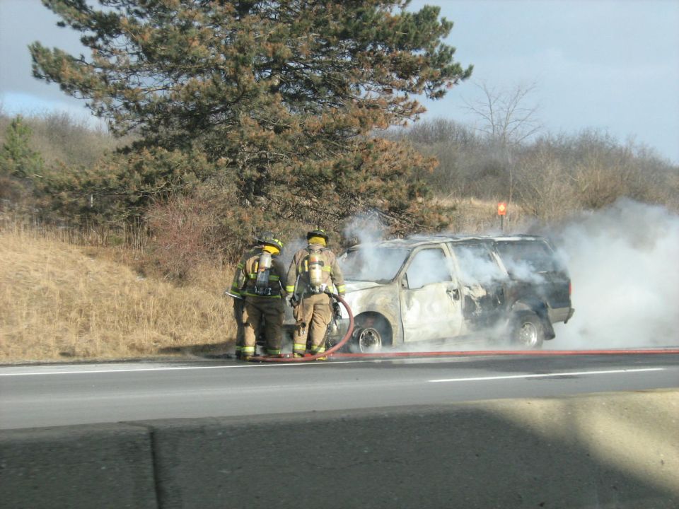 Firefighters extinguishing a burned SUV on highway shoulder
