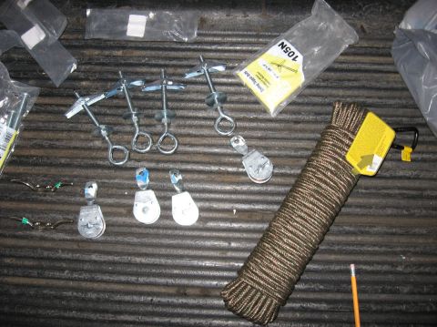 1978 Ford Bronco - Hardware laid out on a ribbed rubber floor mat: zinc eye bolts with toggle-bolt wings, five small metal and plastic rope pulleys, two brass…