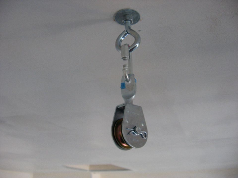 Small metal pulley hanging from a ceiling eye bolt by a snap hook