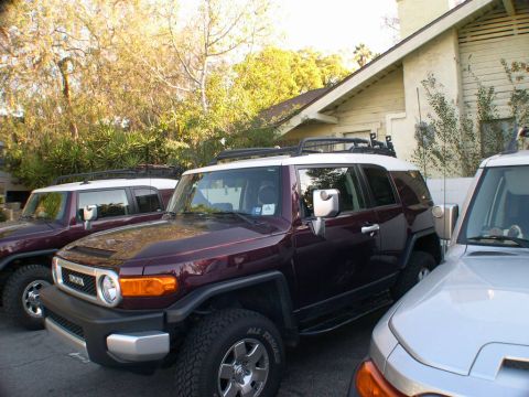 2007 Toyota FJ Cruiser - Two maroon Toyota FJ Cruisers are parked in front of a house, with a silver vehicle to the right.