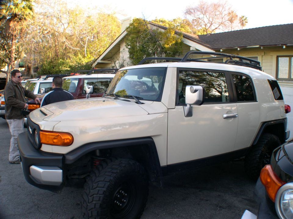 Tan Toyota FJ Cruiser parked in front of a house, with other FJ Cruisers behind it