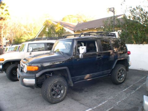 2007 Toyota FJ Cruiser - Two Toyota FJ Cruisers, one black and one white, are parked side-by-side in a lot.