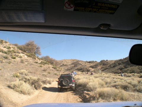 2007 Toyota FJ Cruiser - A convoy of SUVs and ATVs navigates a dusty trail through arid hills under a clear blue sky.