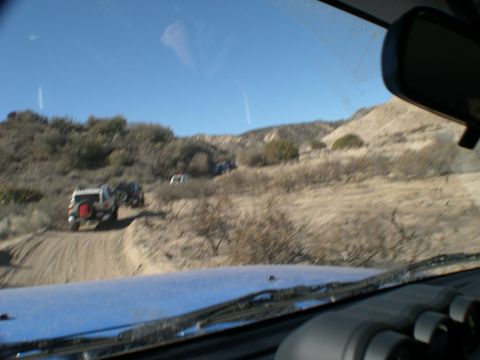 2007 Toyota FJ Cruiser - A convoy of off-road vehicles navigates a winding dirt path through a barren, sun-drenched landscape.
