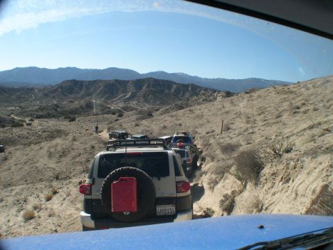 2007 Toyota FJ Cruiser - A convoy of Toyota FJ Cruisers navigates a dusty trail through a mountainous desert terrain under a clear blue sky.