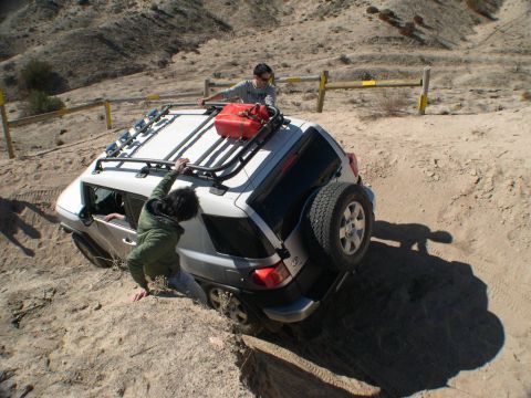 2007 Toyota FJ Cruiser - A white 2007 Toyota FJ Cruiser is stuck in a sandy ditch while two individuals attempt to push it out.
