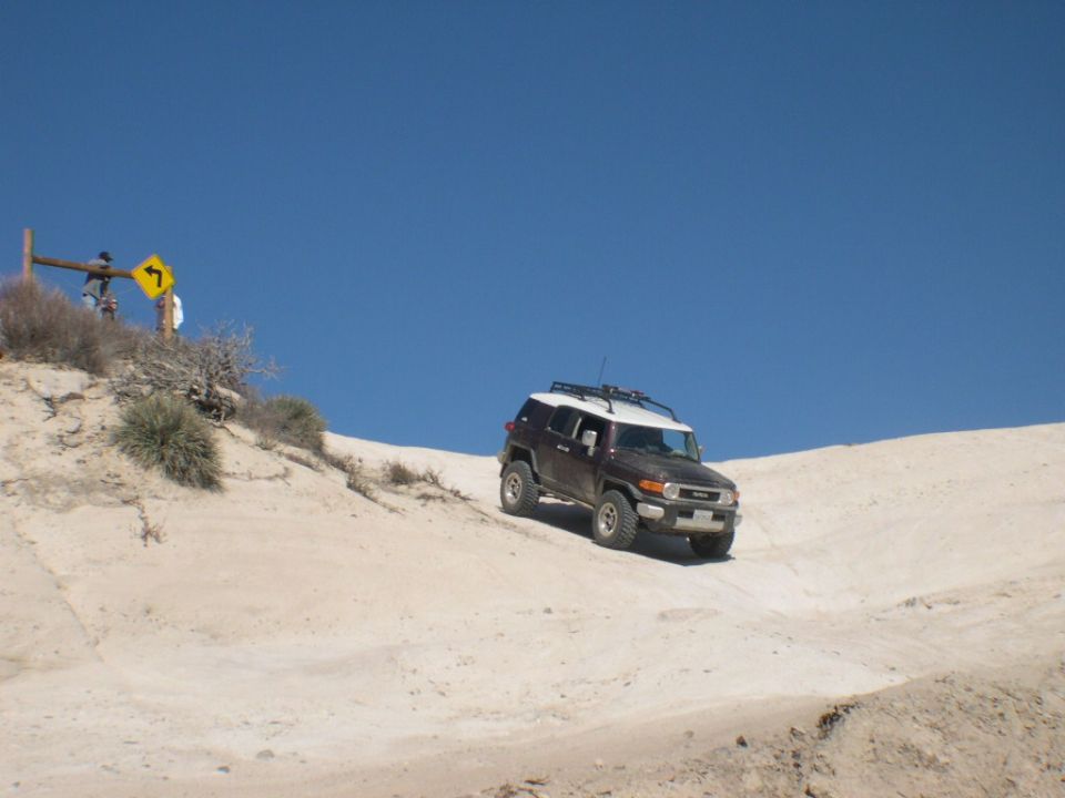 Dark brown 2007 Toyota FJ Cruiser with a white roof and roof rack driving on a sandy hill