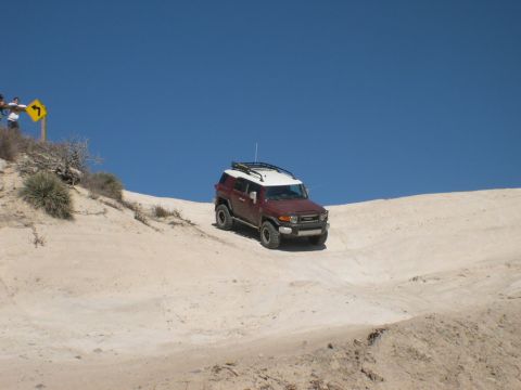 2007 Toyota FJ Cruiser - A red and white 2007 Toyota FJ Cruiser navigates a sandy incline under a clear blue sky.