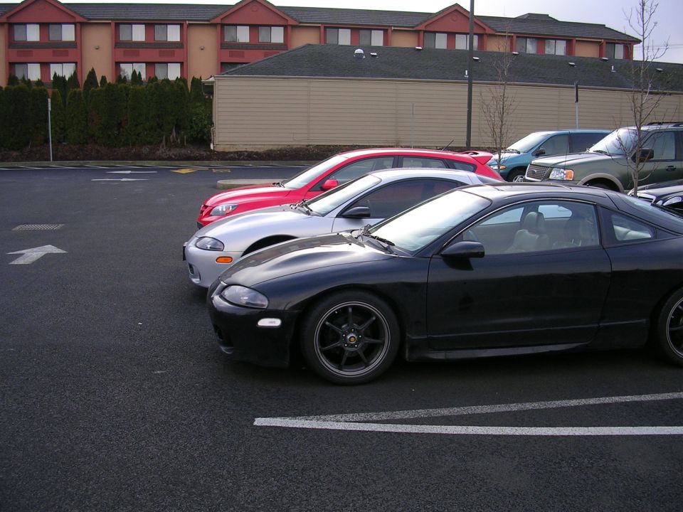 Black sport coupe with dark aftermarket wheels parked beside silver and red coupes in a hotel parking lot