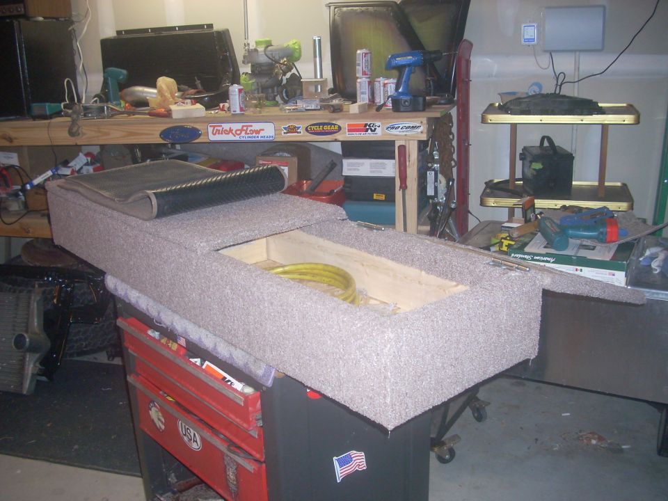 Carpeted storage unit on red toolbox, yellow hose inside, workbench in background